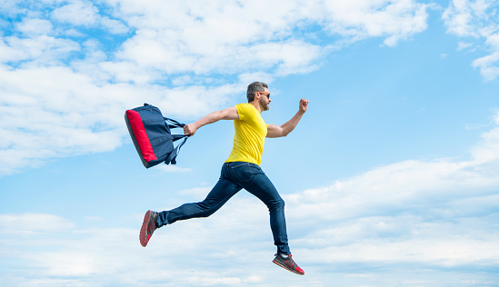 Active man running with sporty bag midair sky background, sport.
