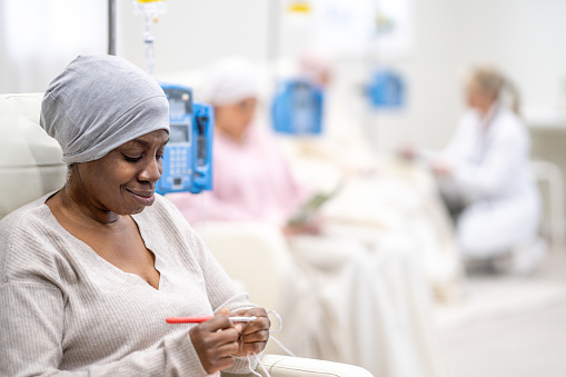 A small group of women are seen sitting in a Cancer clinic as they receive their Chemotherapy intravenously.  They are each dressed comfortably and have blankets and headscarves on to keep them warm.