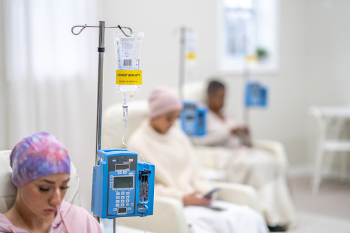 A small group of women are seen sitting in a Cancer clinic as they receive their Chemotherapy intravenously.  They are each dressed comfortably and have blankets and headscarves on to keep them warm.
