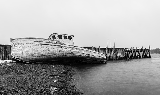 Black and white image of an old abandoned fishing boat alongside dilapidated wharf