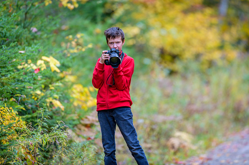 Boy in red shirt taking photo with camera with autumn foliage background