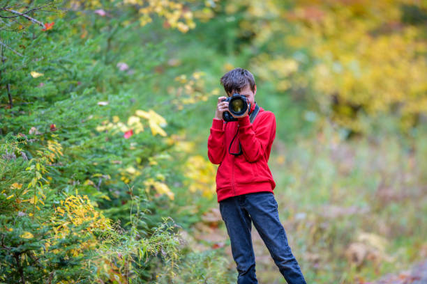Boy in red shirt taking photo with camera with autumn foliage background