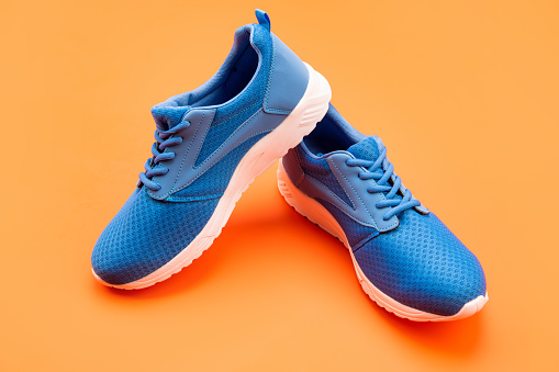 shoe store. shopping concept. footwear for training. athletic footgear for running. pair of comfortable sport shoes. sporty blue sneakers. shoes on orange background.