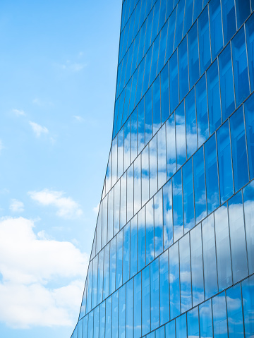 the sky with white clouds reflecting in the glass windows of a modern office building.