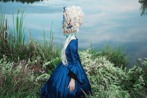 Renaissance princess with blonde hair on lake background.