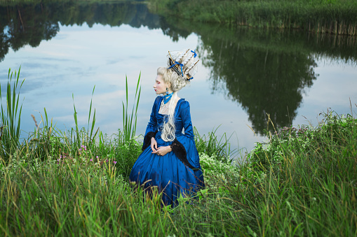 Renaissance princess with blonde hair on lake background.