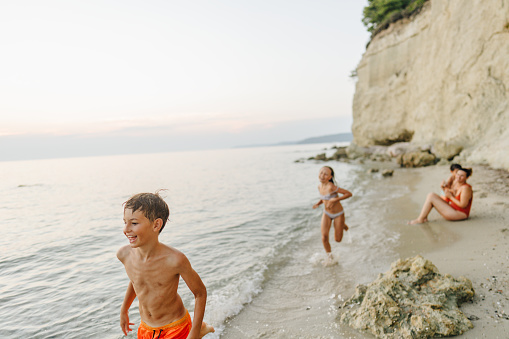 Photo of a little boy, his siblings and their mother, enjoy hot summer afternoon at local beach