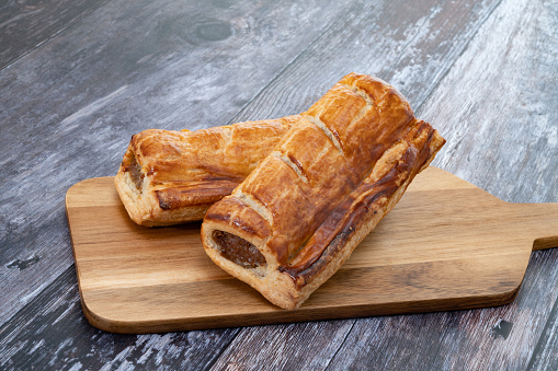 Two sausage rolls on a wooden cutting board