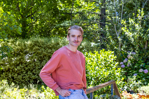 Portrait of 22 years old young man standing in the garden, background with copy space, full frame horizontal composition