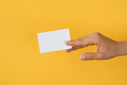 Close-up of a card in a woman's hand isolated on yellow.