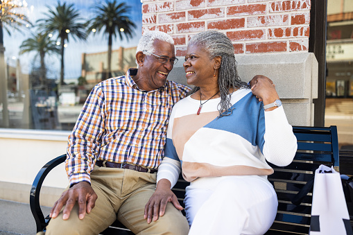 A senior black couple shopping downtown during the daytime sitting on a bench
