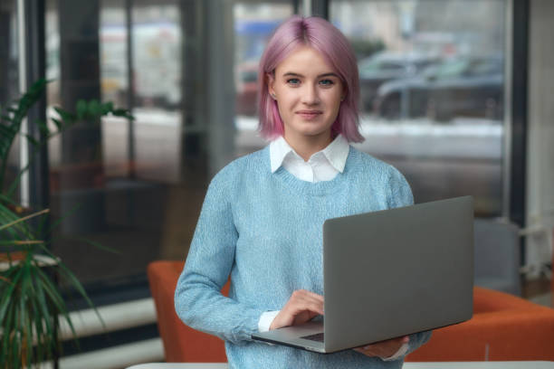 istock Successful young woman student, programmer or entrepreneur holds laptop, stands in modern office or coworking looking at the camera and smiling 1462795050
