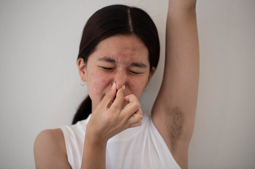Teenage girl her nose with her hands because she was sweating in her armpits and had a bad smell. Health care concept.