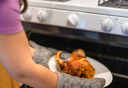 A woman cooking a chicken and checking the temperature using a digital thermomter