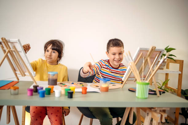 Two kids having fun on painting class Two children sitting on desk and enjoy creating painting art and craft product stock pictures, royalty-free photos & images