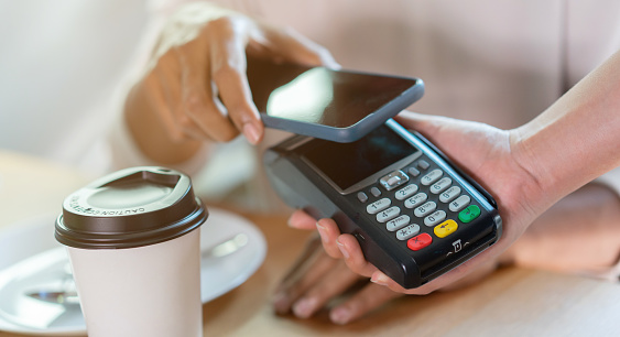 Lector de pagos sin contacto de cerca en la mano de la camarera Escanee al cliente desde el teléfono inteligente hasta el pago de la factura en la mesa en el concepto de transacción de tecnología Café FR photo