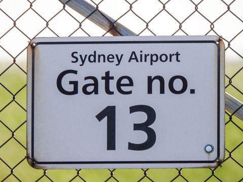 Sign on Gate 13 of Sydney Kingsford-Smith Airport.  This image faces west and in the background is the setting sun.  Also visible is the grass areas around the main runway and apron.  The \