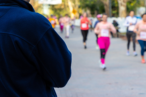 A person watches women run down a street during a charity 5k road race.
