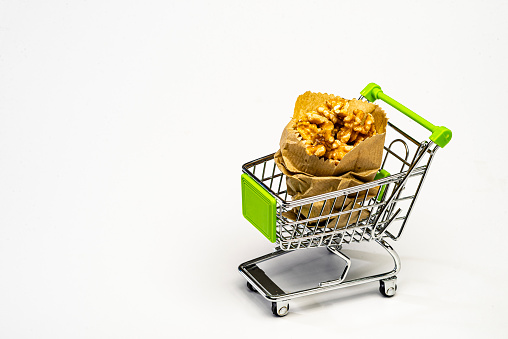 Walnuts in paper bag in shopping cart over white background. Conceptual image to buy by internet.