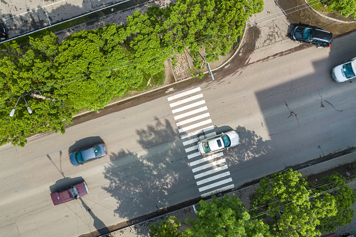 Top down aerial view of busy street with moving cars traffic and zebra road pedestrian crosswalk.