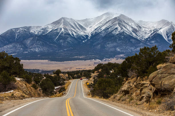 istock Open country road with snow capped mountains in background during winter 1462903571