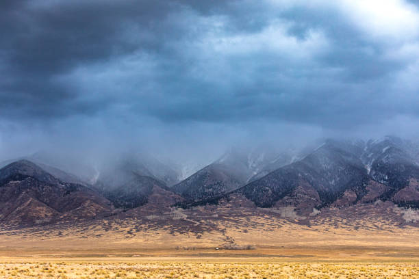 istock Dramatic storm clouds and rain moving over flat farmland and snowy mountains 1462903608