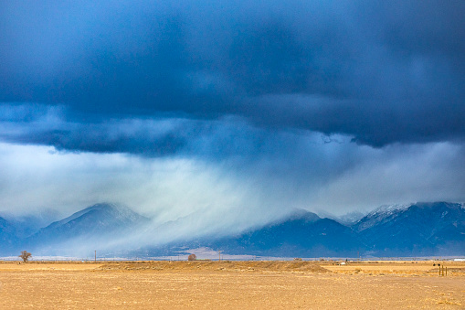 Dramatic storm clouds and rain moving over flat farmland and snowy mountains. Winter weather scene in the USA.