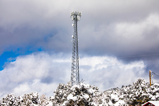 5G cell communication tower surrounded by snow covered trees and dramatic sky in background