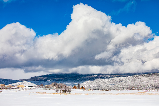 Trees and snow covered land in winter with mountains and dramatic sky in background. Idyllic winter weather scene in USA.
