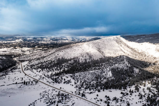 istock Open country road surrounded by snow with snow capped mountains in background 1462904164