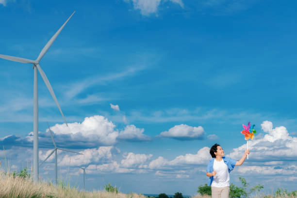 niño asiático progresivo jugando con un juguete de molinete de viento en una granja de turbinas eólicas. - run of the mill fotografías e imágenes de stock