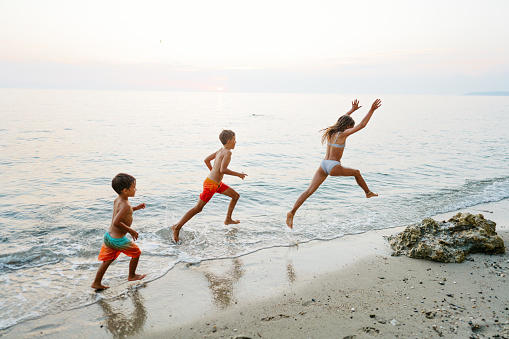 Photo of a little boy and his two siblings, older brother and sister, enjoy hot summer afternoon at local beach