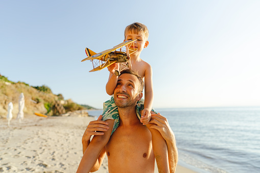 Photo of a little boy and his dad on the beach. Boy is holding a model of plane and shows how it flies.