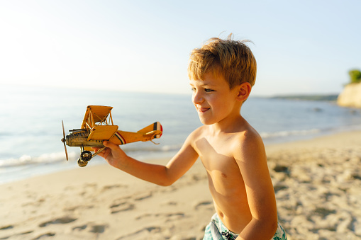 Photo of a little boy playing with an airplane toy at the beach