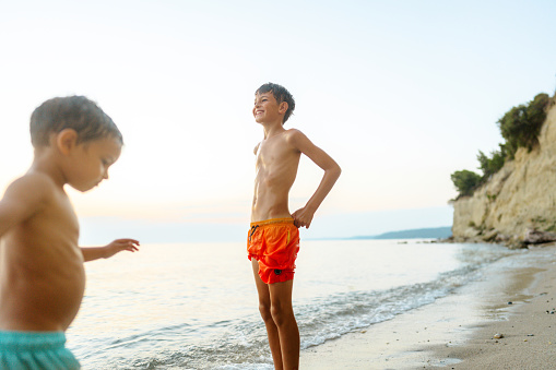 Cute little caucasian boy from behind cheering with arms outstretched while sitting on his father's shoulders at the beach. Playful young child from the back having fun and bonding with dad outdoors. The innocence of childhood.