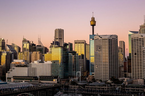 A distance photo of Sydney's city districts towards the end of sunset with glorious pink and mauve tones in the sky reflecting off the glass buildings and the water.