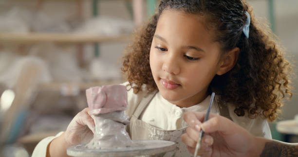 istock Workshop, craft and girl learning to paint in art or pottery class as development for a child. Kid, teacher and curious about painting at artistic or design school for an assessment as education 1462929977