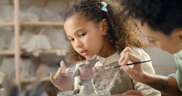 istock Art, creative and girl learning to paint in a craft workshop or pottery class as development for a child. Kid, teacher and curious about painting at artistic or design school for an assessment 1462932987