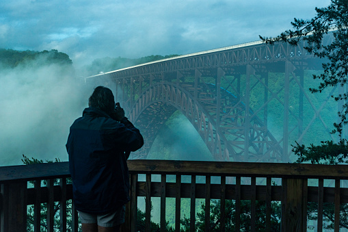 Man photographs the New River Gorge Bridge in clouds and fog early morning, West Virginia, USA