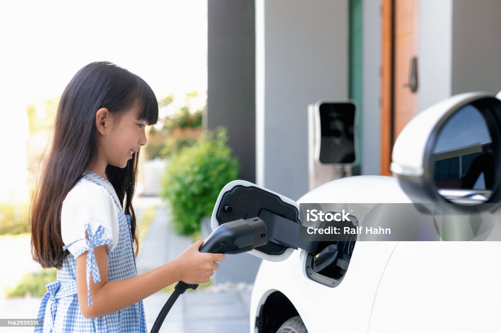 Sustainable power source for progressive lifestyle shown by a girl hold EV plug A playful girl holding an EV plug, a home charging station providing a sustainable power source for electric vehicles. Alternative energy for progressive lifestyle. Electric Vehicle Stock Photo