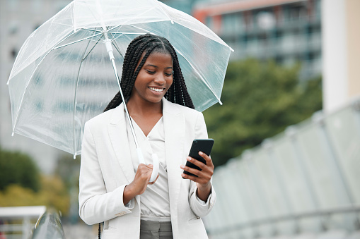 Business, black woman and smartphone, city and rain with umbrella, communication with technology and smile, travel and commute to work. Professional, urban mockup and online with worker in Chicago.