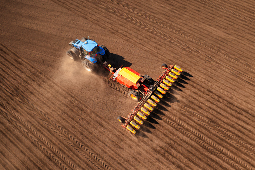 A tractor with a seeder on the field drone view, the spring season of the sowing campaign.