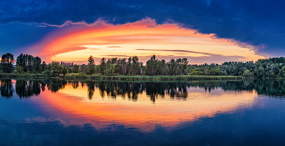 Sunset on the lake. Orange clouds on the background of the blue sky are illuminated by the sun. A wonderful summer evening. Landscape panorama.
