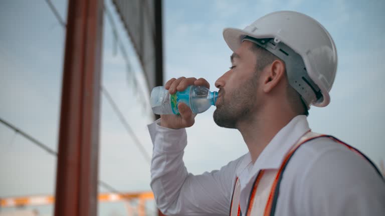 An engineer man wearing protective clothing stands drinking water.