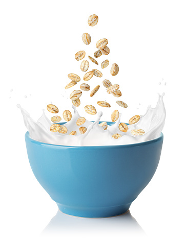 oatmeal falling in blue bowl with splashing milk isolated on white background