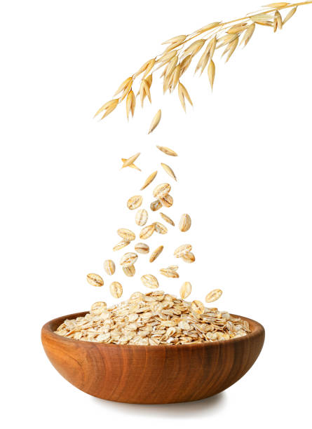 farina d'avena che cade dalle orecchie d'avena in ciotola isolata su bianco - oat oatmeal rolled oats oat flake foto e immagini stock