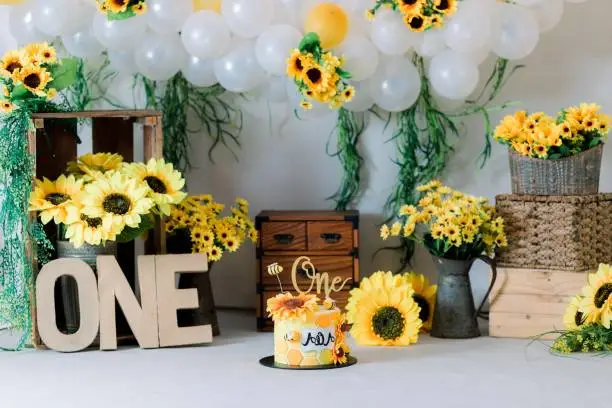 Photo of Bee theme first birthday cake with sunflowers and balloons