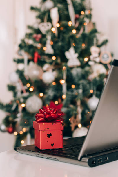 istock Small red present with gift bow next to laptop on table in front of decorated christmas tree 1462968974