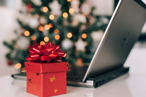 istock Small red present with gift bow next to laptop on table in front of decorated christmas tree 1462968979