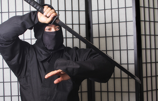 An Asian man wearing ninja costume and holding weapons